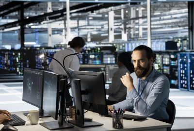 Technician using PC in data center to update server tech, configuring equipment using software tools. Server room employee reviewing hardware analytics, ensuring reliable network operations